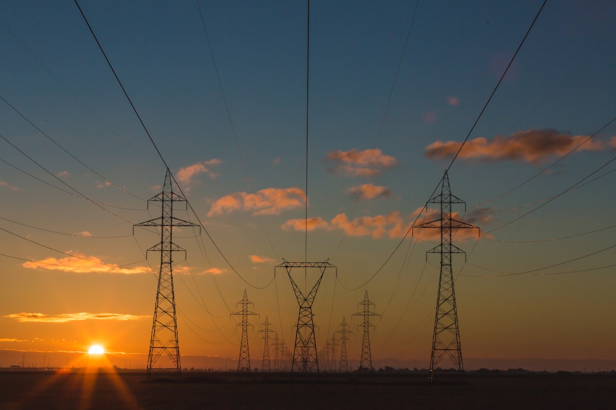 Electricity transmission pylons silhouetted against a warm sunset sky
